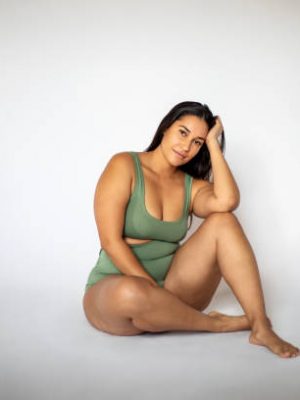 gettyimages-1220401218-612×612 Portrait of a beautiful oversize woman in lingerie sitting on white background. Plus size woman in underwear looking at camera with hand on head.